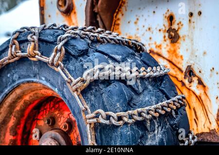Gros plan des roues noires à usage intensif avec des chaînes rouillées d'un ancien bulldozer à neige Banque D'Images