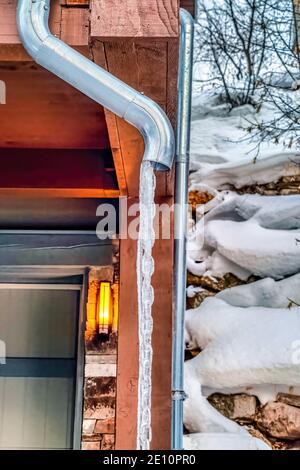 Tuyau d'évacuation de toit de la maison avec de l'eau gelée contre la neige et pente rocheuse Banque D'Images