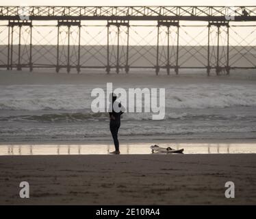 Surfeur debout avec planche de surf à la plage de sable de Playa Pimentel avec Muelle Pier en arrière-plan Chiclayo Lambayeque Pérou en Amérique du Sud Banque D'Images