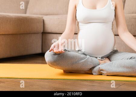 Femme enceinte s'exerçant sur un tapis orange dans la chambre. Grossesse Yoga et Fitness concept à l'heure du coronavirus. Banque D'Images