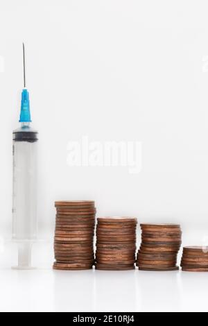 Seringue fot santé concept avec piles de pièces sur fond blanc, affaires, financier et santé, concept de vaccination. Banque D'Images