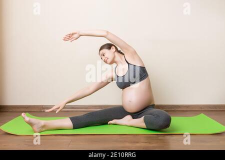 Grossesse Yoga et Fitness concept à l'heure du coronavirus. La femme enceinte médite à l'intérieur dans la pose de yoga. Femme appréciant dans la méditation. Banque D'Images