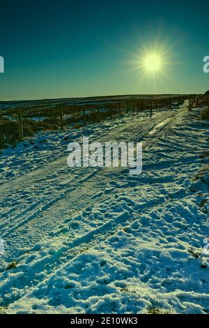 En fin d'après-midi, et un faible soleil illumine une piste de moorland enneigée dans le Yorkshire Banque D'Images