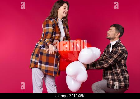 Une femme satisfaite reçoit un bouquet de ballons sous forme de coeurs de son petit ami sur fond rouge. Photo de haute qualité Banque D'Images