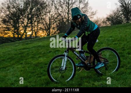 Londres, Royaume-Uni. 3 janvier 2021. Une femme VTT descend une colline avec son chien en panne - Londres est au niveau 4 (LockDown 3) et Primrose Hill est occupé, malgré le froid, la pluie, le grésil et la grêle, tandis que les gens cherchent de l'air frais et de l'exercice. Crédit : Guy Bell/Alay Live News Banque D'Images