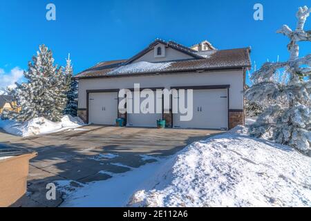 Garage pour trois voitures avec portes blanches et allée enneigée une journée d'hiver ensoleillée Banque D'Images