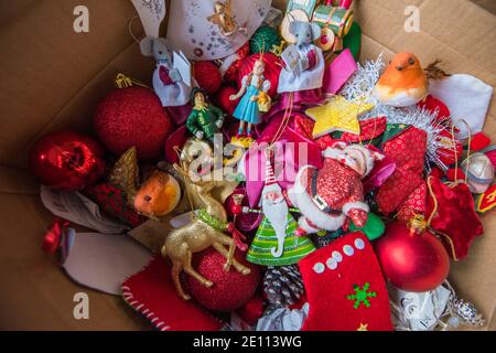 Boîte en carton marron avec un ensemble de Noël coloré en famille décorations d'arbre devant un brûleur en rondins sur une pierre le sol est emballé Banque D'Images