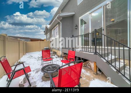 Patio enneigé avec foyer et chaises rouges arrière-cour de la maison par jour nuageux Banque D'Images