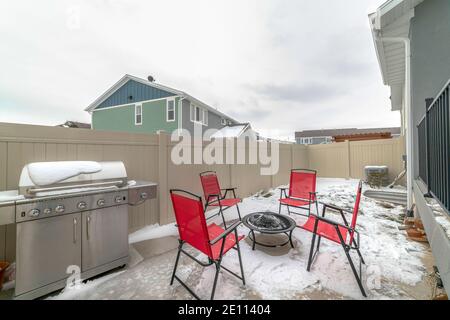 Patio clôturé de la maison avec barbecue et chaises rouges autour d'un foyer Banque D'Images