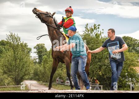 Magdeburg, Allemagne - 24 juin 2017 : des jockey se promeuneurs à cheval jusqu'à l'hippodrome. Deux assistants l'aident. Circuit de course à Magdeburg Banque D'Images