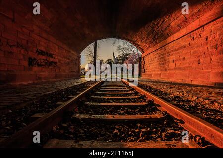 Vieux tunnel avec chemin de fer dans la soirée au coucher du soleil. Horizon de Francfort à la sortie du tunnel. Parc avec arbres et prairie au printemps avec fleurs Banque D'Images