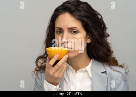 Femme d'affaires malade essayant de sentir l'odeur de la moitié d'orange frais, a des symptômes de Covid-19. Banque D'Images