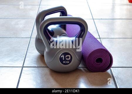 Deux poids kettlebell de 10 kg et tapis de yoga violet sur le sol Banque D'Images