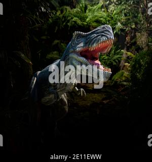 Vue en gros plan d'une figurine de dinosaure en colère T-Rex dans la jungle. Animal monstrueux à bouche ouverte et dents acérées Banque D'Images