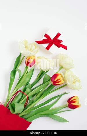 Tulipes rouges et jaunes dans un sac cadeau rouge et un cadeau sur fond blanc avec espace de copie. Carte de vœux de Saint-Valentin ou de fête des mères Banque D'Images