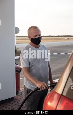 homme dans un masque de protection noir ravitailler une voiture à une station-service, protection contre les virus Banque D'Images