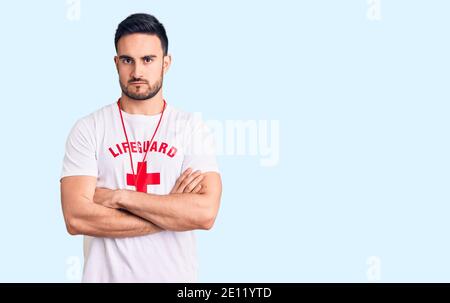 Jeune homme beau portant un maître-nageur uniforme sceptique et nerveux, désapprouvant l'expression sur le visage avec les bras croisés. Personne négative. Banque D'Images