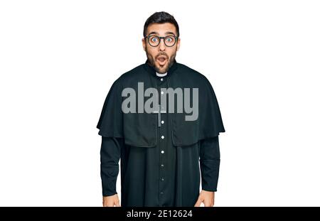 Jeune homme hispanique portant l'uniforme de prêtre effrayé et étonné de la bouche ouverte pour la surprise, incrédulité visage Banque D'Images