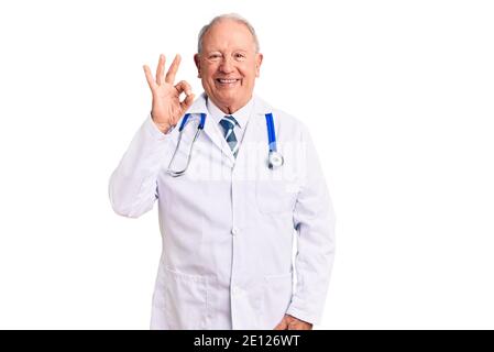 Senior beau gris-cheveux homme portant le docteur manteau et stéthoscope sourire positif faire signe ok avec la main et les doigts. Expression réussie. Banque D'Images