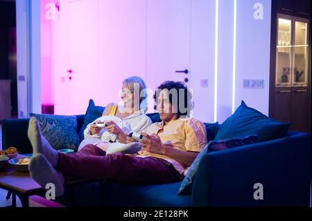 Un jeune couple heureux jouant à un jeu vidéo assis à la maison sur un canapé pendant l'auto-isolement en quarantaine. Banque D'Images