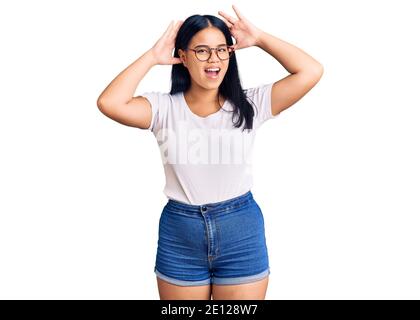 Jeune fille asiatique belle portant des vêtements et des lunettes décontractés souriants gai jouer un puavoir avec les mains montrant le visage. Surpris et sorti Banque D'Images