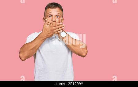 Beau muscle homme portant décontracté blanc tshirt choqué couvrant la bouche avec les mains pour erreur. Secret concept. Banque D'Images