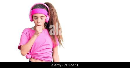 Mignon enfant hispanique fille portant des vêtements de gym et utilisant des écouteurs se sentir mal et la toux comme symptôme de froid ou de bronchite. Concept de soins de santé. Banque D'Images