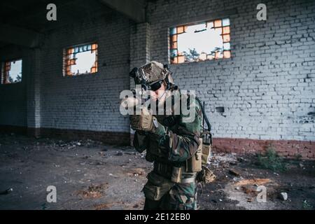 Un soldat des forces spéciales marchant avec un fusil d'assaut dirigé dans un bâtiment détruit. Banque D'Images