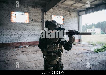 Un soldat des États-Unis à part entière, MARSOC, armé d'un fusil d'assaut, traverse le bâtiment abandonné. Affrontement militaire. Banque D'Images