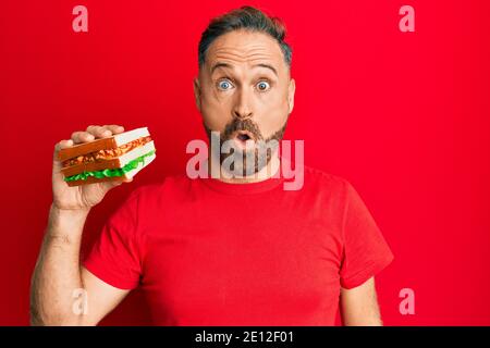 Beau homme d'âge moyen mangeant sandwich peur et stupéfié avec la bouche ouverte pour la surprise, le visage incrédulé Banque D'Images