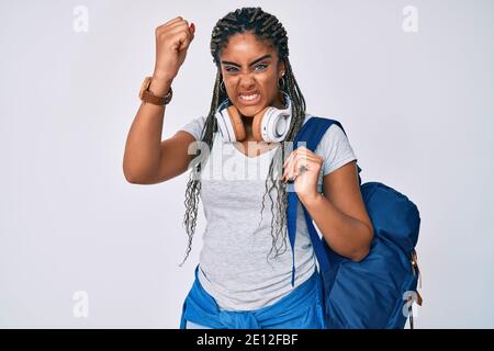 Une jeune femme afro-américaine avec des tresses portant un sac à dos et un casque d'étudiant agacé et frustré criant avec colère, hurlant fou de colère Banque D'Images