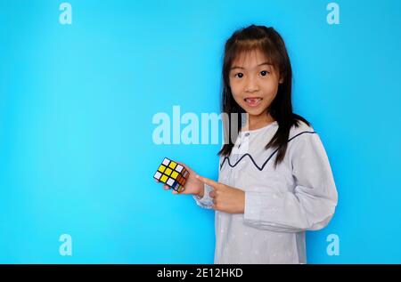 Une jeune fille asiatique mignonne joue avec un cube de Rubik, s'amusant tout en apprenant. Fond bleu clair Uni. Banque D'Images