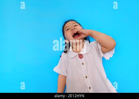 Une jeune fille asiatique mignonne se sentant excitante, criant du haut de ses poumons avec sa bouche large ouverte et une paume près de sa bouche. Fond bleu clair Uni Banque D'Images