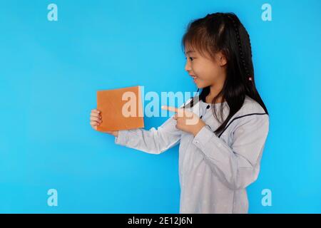 Une jeune fille asiatique mignonne debout sur un fond bleu clair Uni, tenant un morceau de papier vierge, souriant. Banque D'Images