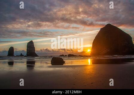 Coucher de soleil à Cannon Beach, Oregon, avec Haystack Rock et les aiguilles dominant la vue avec des nuages à appliqué de roses au-dessus. Banque D'Images