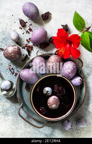 Jaune d'œuf de Pâques naturel violet. Les œufs faits maison sont peints avec un colorant naturel provenant de fleurs d'hibiscus séchées sur une table en pierre grise. Plan d'étapage avec vue de dessus Banque D'Images