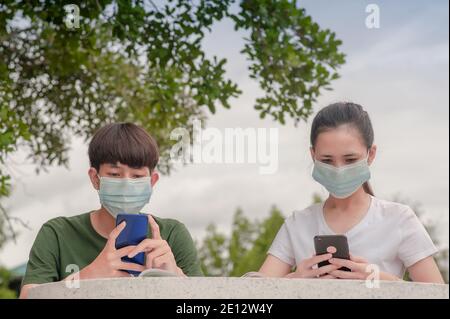 Garçon et fille dans masque nouveau normal en utilisant mobile smartphone garder la distance sociale protéger le coronavirus covid 19 Banque D'Images