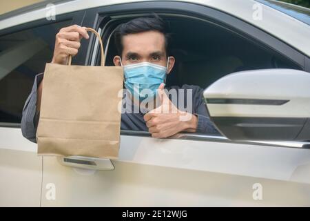 Homme asiatique porter un masque de visage tenant un sac de shopping assis dans Voiture, masque protéger le coronavirus covid 19 Banque D'Images