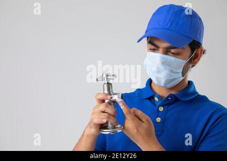 UN PLOMBIER PORTANT UN MASQUE FACIAL POUR RÉPARER UN ROBINET CASSÉ Banque D'Images