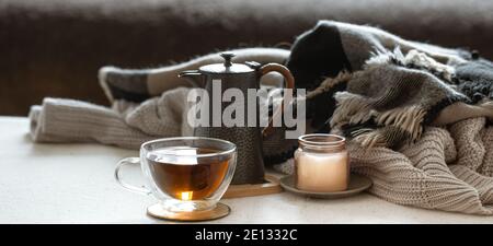 Encore la vie avec une tasse de thé, une théière, une bougie dans un chandelier et des choses tricotées gros plan. Banque D'Images