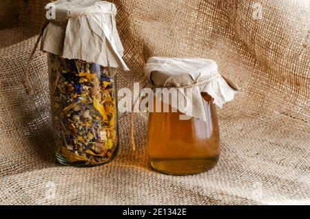 Herbes médicinales et médecine alternative concept.Herbal herbes séchées médicinales et miel d'abeille. Thé de fleur séché et miel liquide cru dans des pots en verre sur toile de jute. Banque D'Images