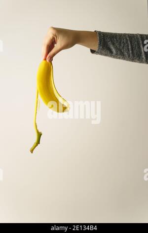 Main d'une femme caucasienne inconnue portant une peau de banane devant de mur blanc - espace de copie concept de fin et terminez les déchets prêts à être jetés Banque D'Images