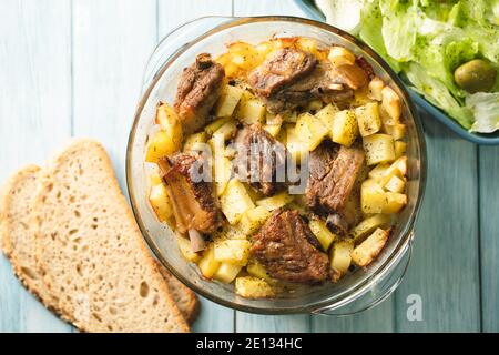 Vue en angle sur le bol avec les pommes de terre et les côtes de viande salade et pain sur table Banque D'Images