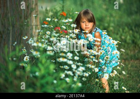 Une petite fille posant dans la cour d'une maison de campagne parmi les fleurs. Banque D'Images