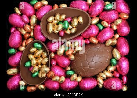 Pile ou groupe de plusieurs couleurs et différentes tailles d'oeufs de pâques au chocolat enveloppés d'une feuille colorée dans le rose, le rouge, l'or et le vert lime avec deux moitiés o Banque D'Images