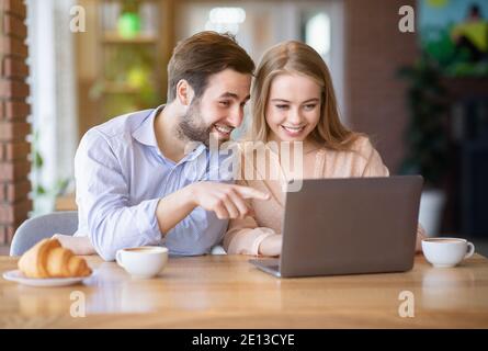 Jolie jeune femme et son petit ami qui navigue sur le Web ou regarder un film sur ordinateur portable au café, panorama Banque D'Images