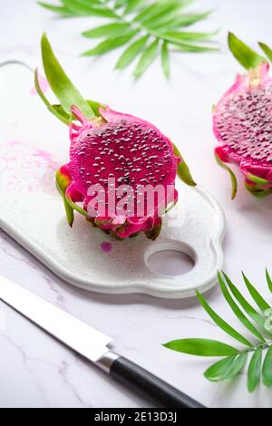 Fruit de dragon rose, pitaya ou pitahaya coupé en cubes sur plaque blanche. Ingrédient super-alimentaire tendance. Gros plan avec planche à découper et couteau. Banque D'Images