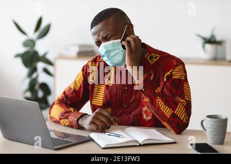 Homme noir stressé en masque médical de protection se grattant le visage, ayant la peau qui démange Banque D'Images