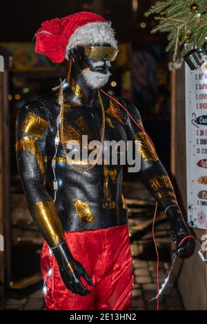 Mannequin d'un homme noir en chapeau rouge et santaclaus shorts et gerlands Banque D'Images