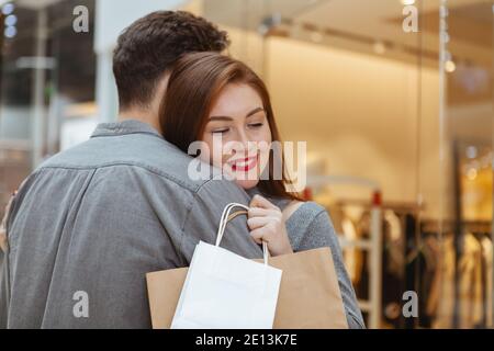 Adorable jeune couple aimant qui s'embrasse dans le centre commercial, l'espace de copie. Magnifique femme souriant avec ses yeux fermés, embrassant son petit ami, tenant s Banque D'Images